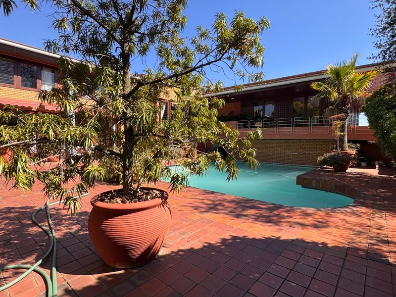 Outdoor pool area featuring brick paving, a swimming pool, and a raised balcony with metal railings, set against a brick residential facade.