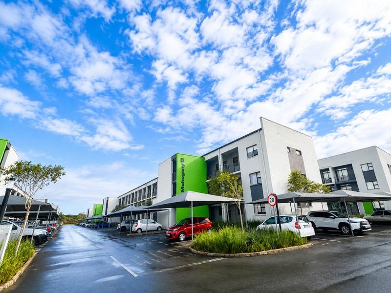 Exterior view of a modern apartment complex featuring covered parking bays, paved driveways, and landscaped garden areas.
