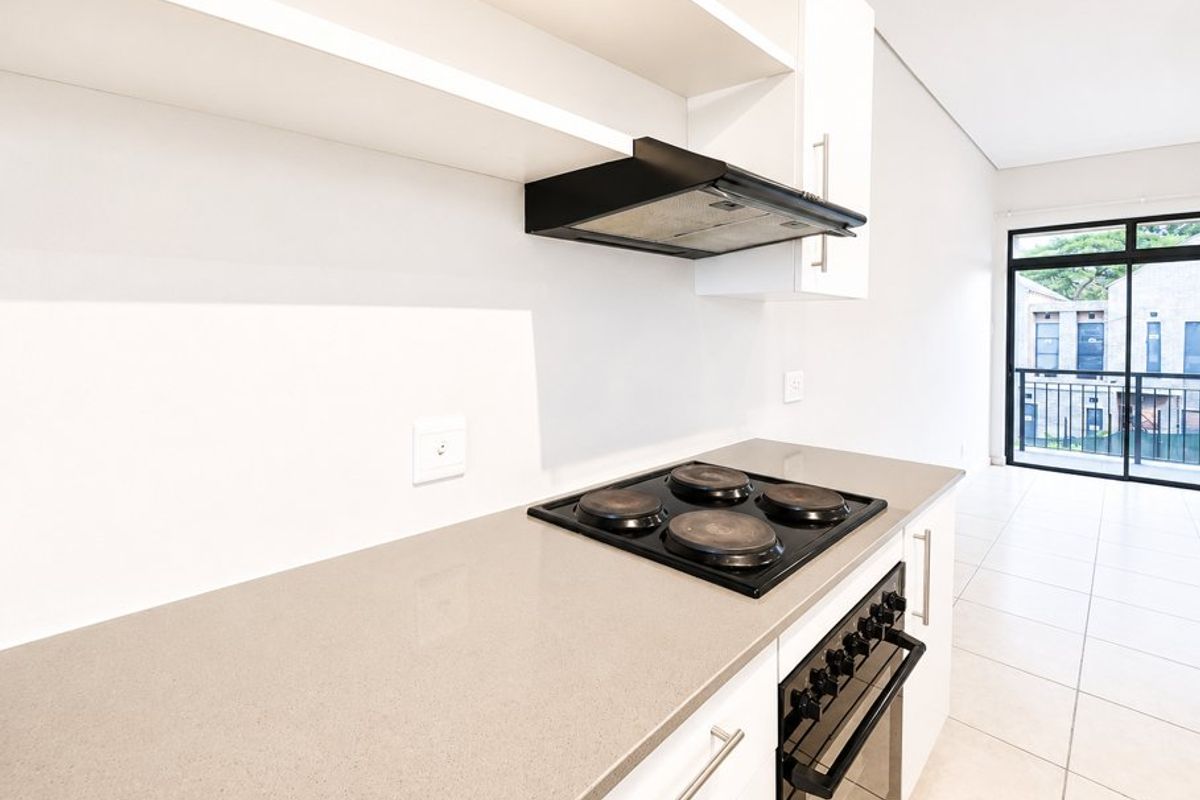 Modern kitchen featuring built-in oven, electric hob, extractor fan, and stone countertops, leading to an open-plan living area with balcony access.