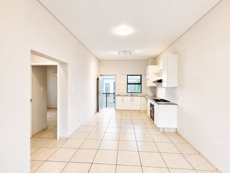 An open-plan kitchen and living area featuring neutral tiled flooring, modern white cabinetry, and direct access to a balcony.
