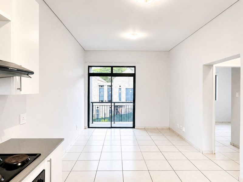 An open-plan kitchen and living area featuring tiled floors, modern cabinetry, and a sliding door leading to a balcony.
