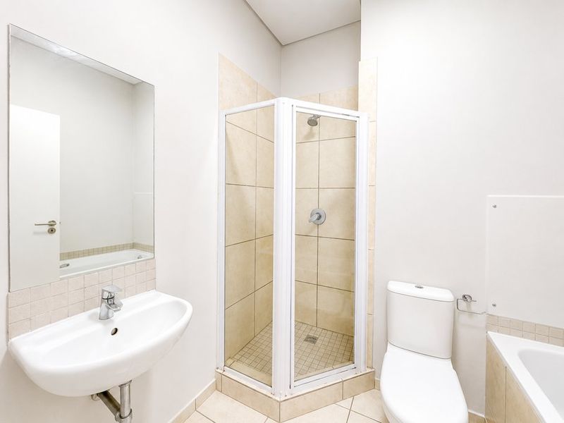 A clean, functional bathroom featuring a corner shower enclosure, wall-mounted basin, toilet, and a bathtub with neutral tiling.