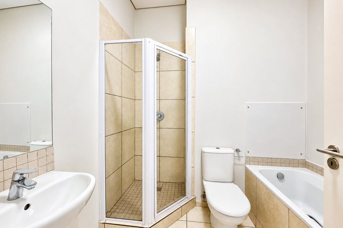 A clean, functional bathroom featuring a separate shower enclosure, bathtub, toilet, and wall-mounted washbasin with neutral tiling throughout.