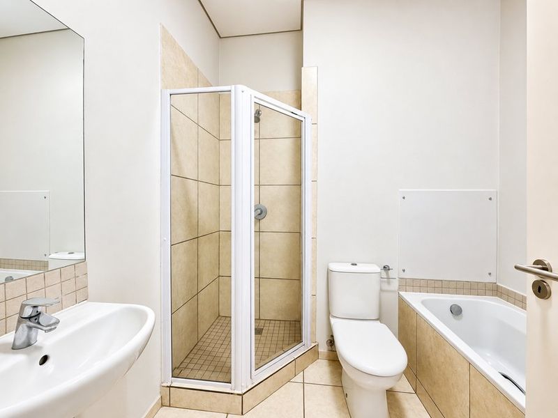 A clean, functional bathroom featuring a separate shower enclosure, bathtub, toilet, and wall-mounted washbasin with neutral tiling throughout.