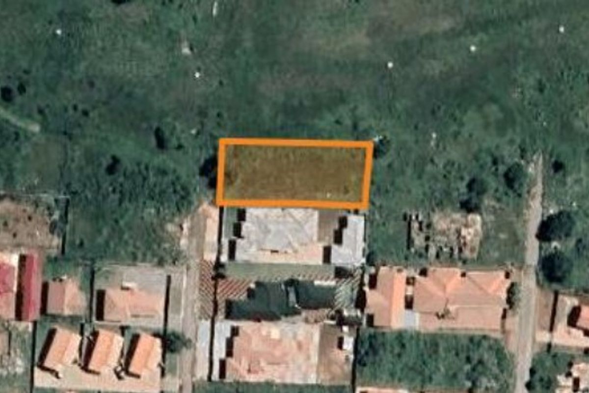 An aerial view of a vacant residential land plot highlighted in an orange boundary within a suburban neighborhood.