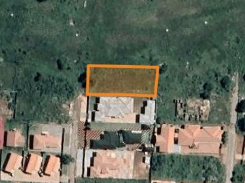 An aerial view of a vacant residential land plot highlighted in an orange boundary within a suburban neighborhood.