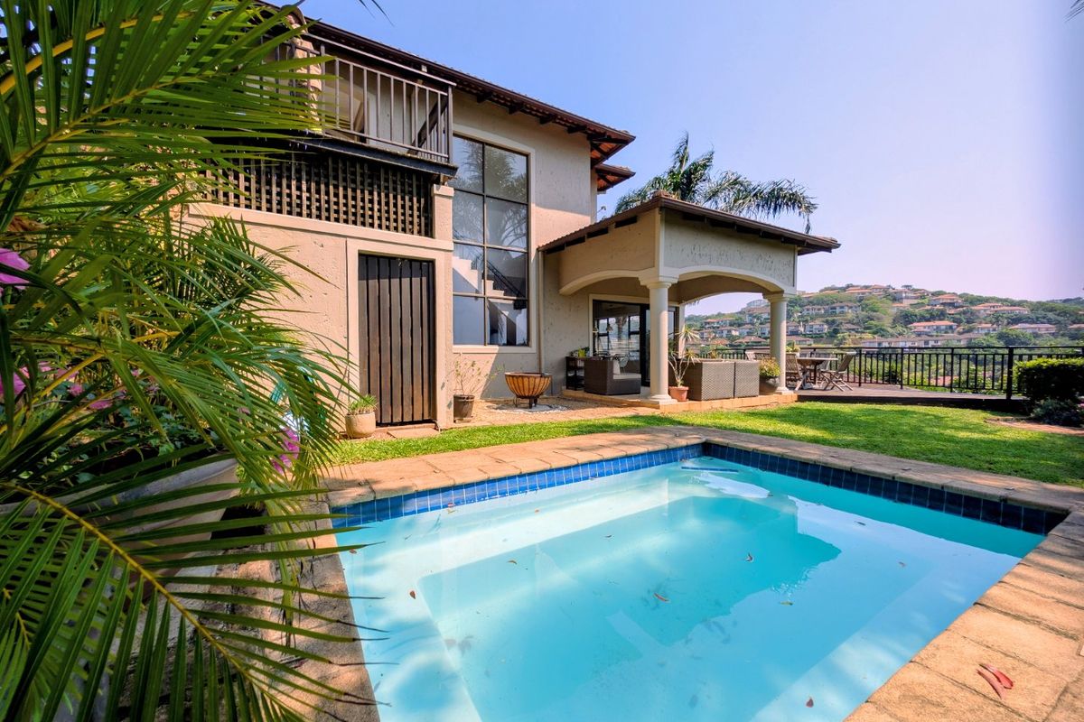 Rear exterior view of the townhouse featuring a private swimming pool, covered patio area, and an upper-level balcony overlooking the garden.