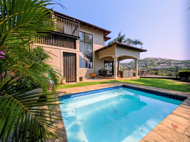Rear exterior view of the townhouse featuring a private swimming pool, covered patio area, and an upper-level balcony overlooking the garden.