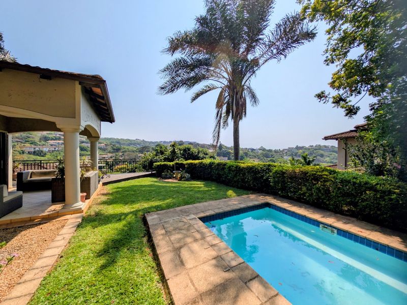 A private outdoor pool area featuring a covered patio, manicured lawn, and scenic views, perfect for relaxation and outdoor entertaining.