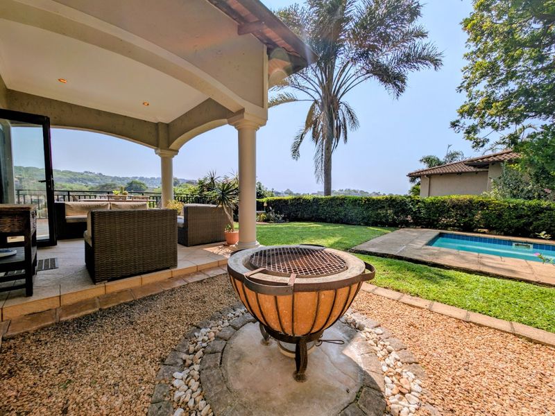 Spacious covered patio overlooking a private swimming pool and landscaped garden, featuring a built-in braai area perfect for outdoor entertaining.