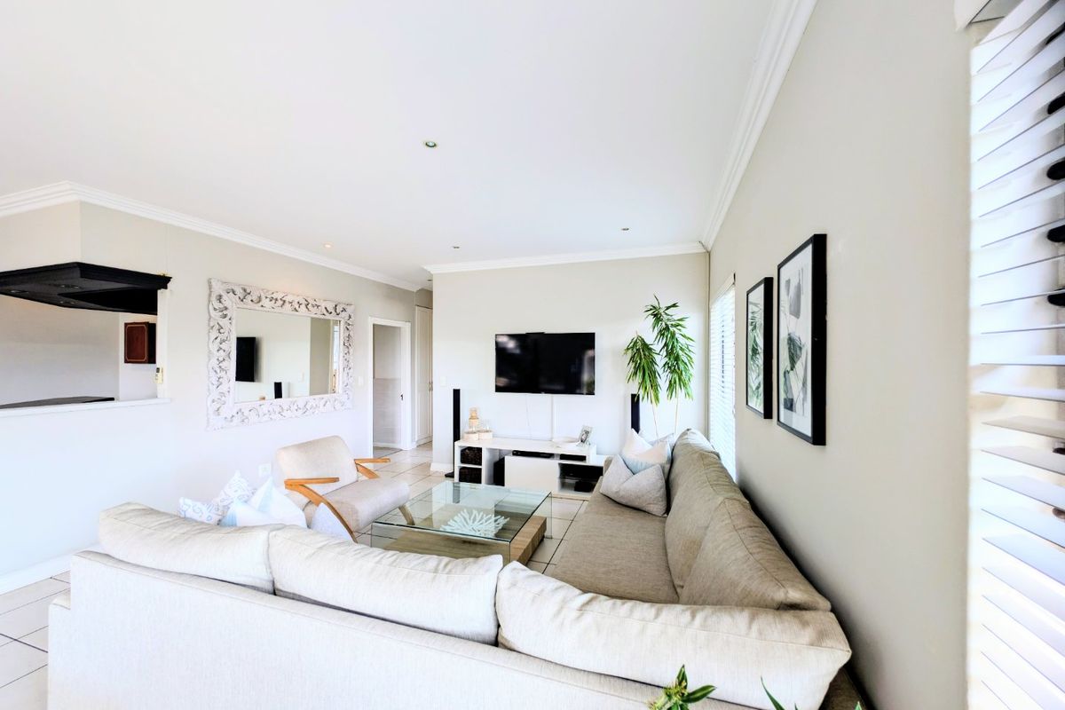 A bright and well-maintained living room featuring neutral tiled flooring, crisp cornicing, and recessed lighting, creating a comfortable and inviting atmosphere.