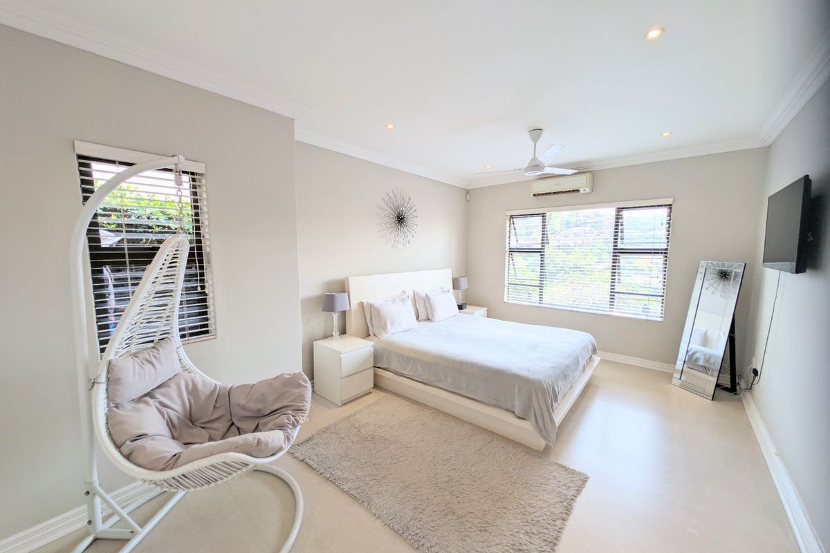 A bright and spacious bedroom featuring neutral tones, a ceiling fan, and a wall-mounted air conditioning unit.