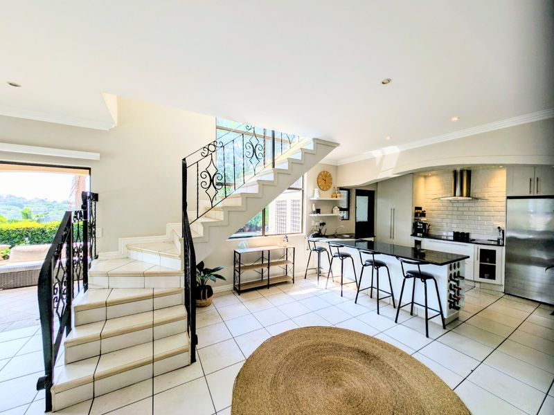 Spacious open-plan living area featuring a modern kitchen with granite island, subway tile backsplash, and a striking tiled staircase with wrought iron detailing.