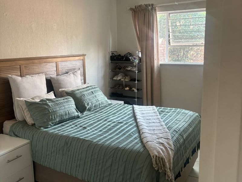 A functional bedroom featuring tiled flooring, a window with security bars, and a neutral wall finish.