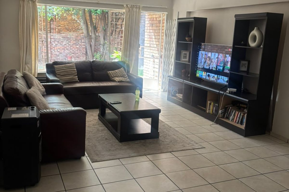A spacious living room featuring tiled flooring, a tongue and groove ceiling, and large windows providing natural light and access to the rear exterior.