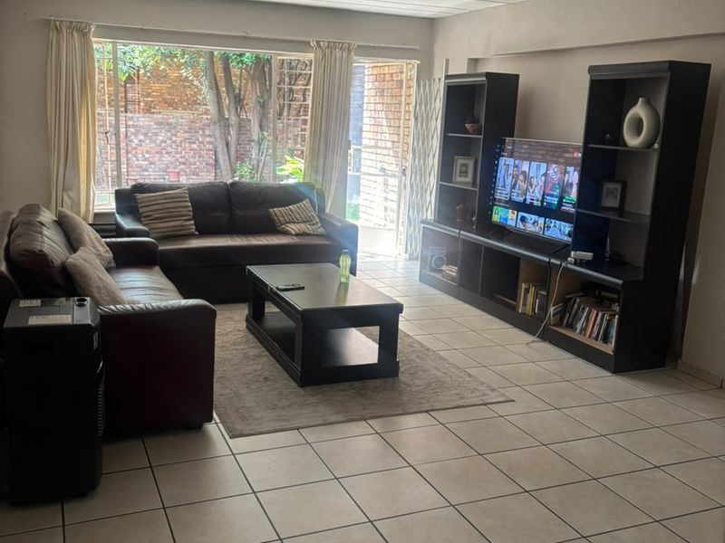 A spacious living room featuring tiled flooring, a tongue and groove ceiling, and large windows providing natural light and access to the rear exterior.