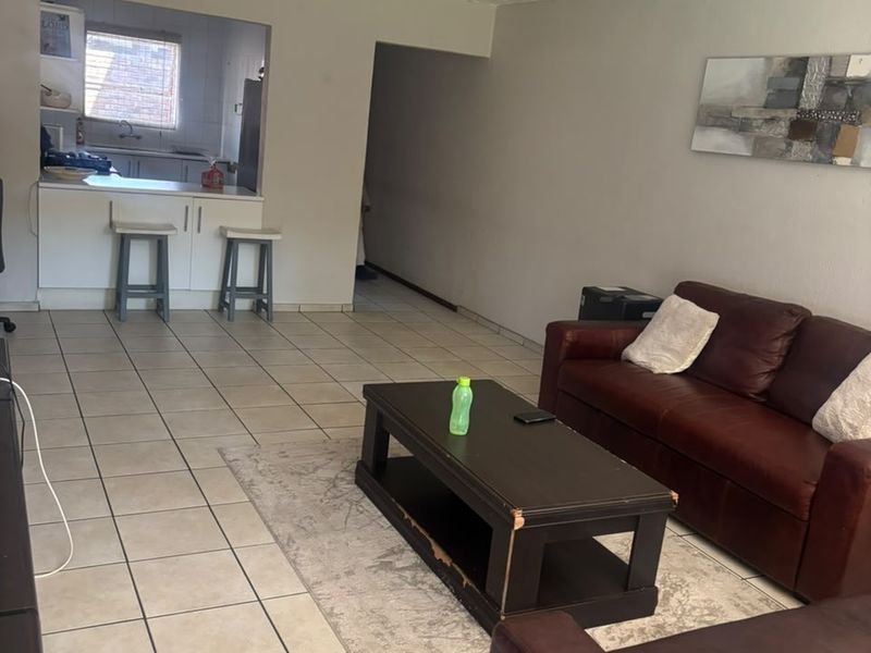 Open plan living area featuring tiled flooring and a tongue and groove ceiling, with a connected kitchen space and breakfast counter.