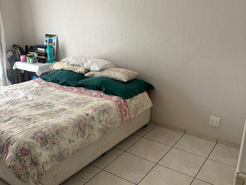 A simple bedroom featuring neutral textured walls and light-colored tiled flooring, providing a functional and blank canvas for potential interior updates.