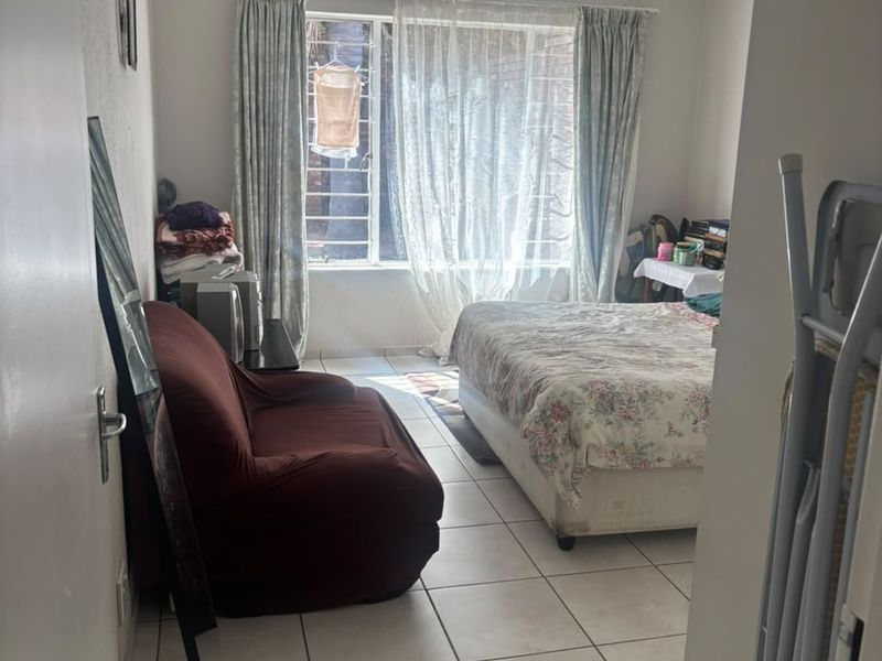 A bedroom featuring tiled flooring, security bars on the window, and ceiling paneling, offering a functional space with natural light.