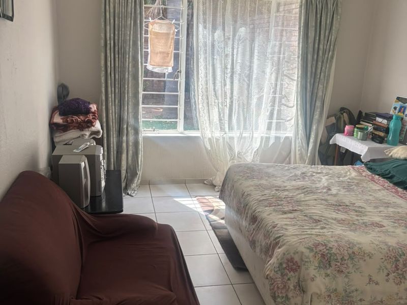 A functional bedroom featuring tiled flooring and a window fitted with security bars, providing natural light and a view of the exterior.