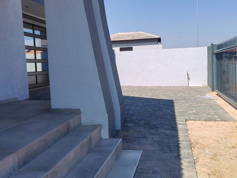 Front entrance area featuring tiled steps, paved driveway, and secure perimeter walling with metal fencing.