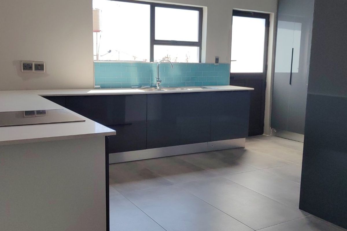 Modern kitchen featuring sleek dark cabinetry, stone countertops, a vibrant blue subway tile backsplash, and large format floor tiles.