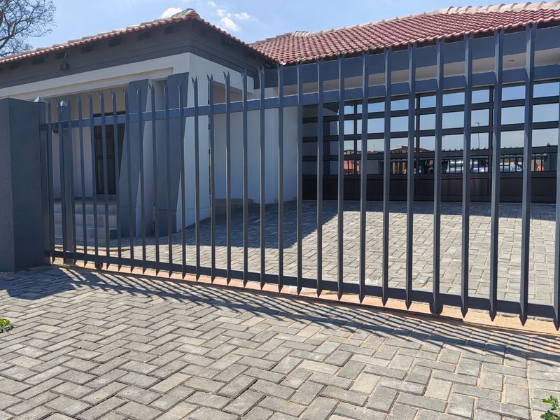 Front exterior view of the property featuring a paved driveway, secure metal fencing, and a modern sliding gate entrance.