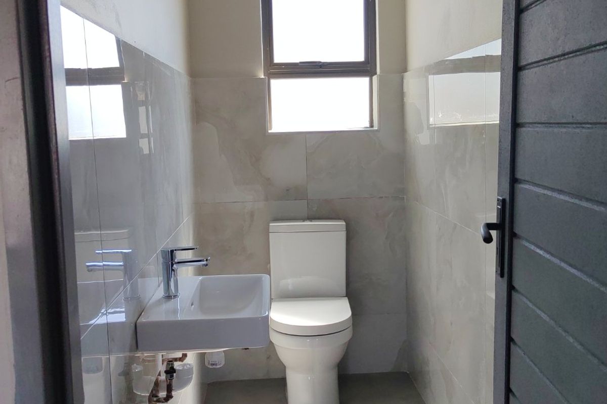 A modern, compact guest bathroom featuring neutral wall tiles, a wall-mounted basin, and a clean, minimalist design.