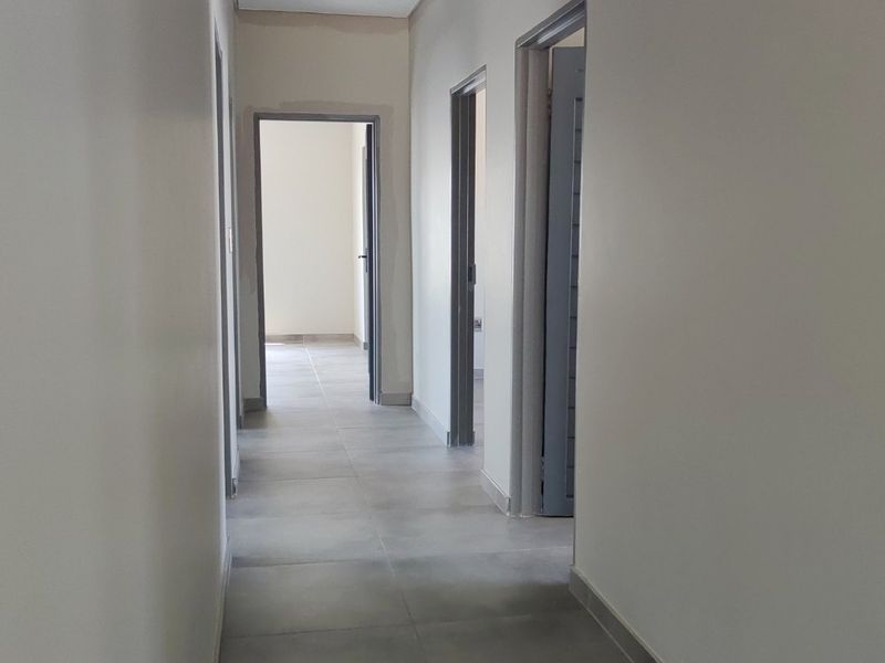 A clean, modern hallway featuring neutral tiled flooring and multiple doorways leading to adjacent rooms, currently in a vacant, move-in ready state.