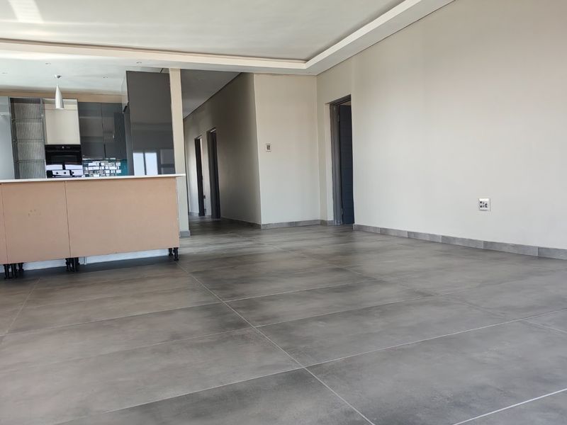 An open-plan living and kitchen area featuring large format grey floor tiles, recessed ceiling lighting, and a partially finished kitchen island.