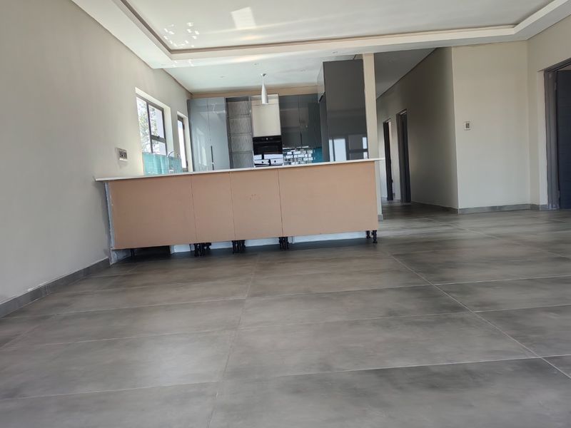 Open plan kitchen area featuring modern grey cabinetry, a central island, and large format floor tiles. The space is currently unfinished.
