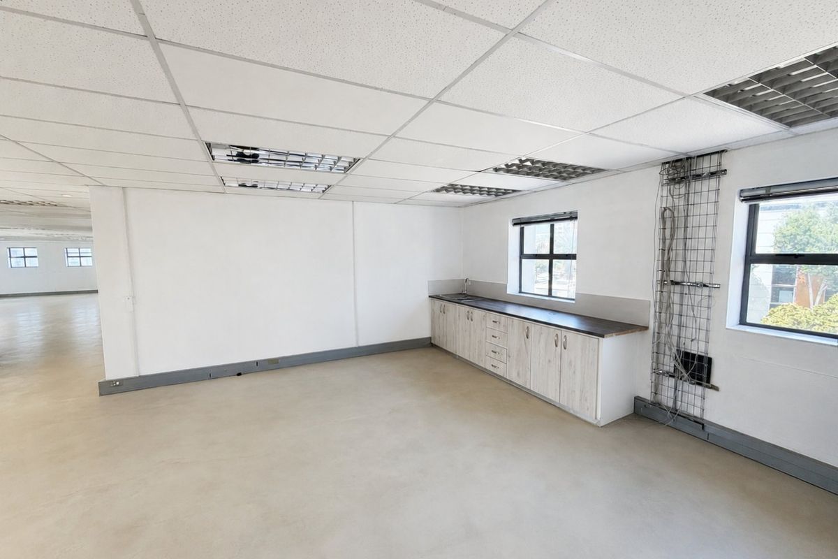 Open-plan commercial office space featuring a built-in kitchenette, polished concrete floors, and suspended ceiling with recessed lighting.