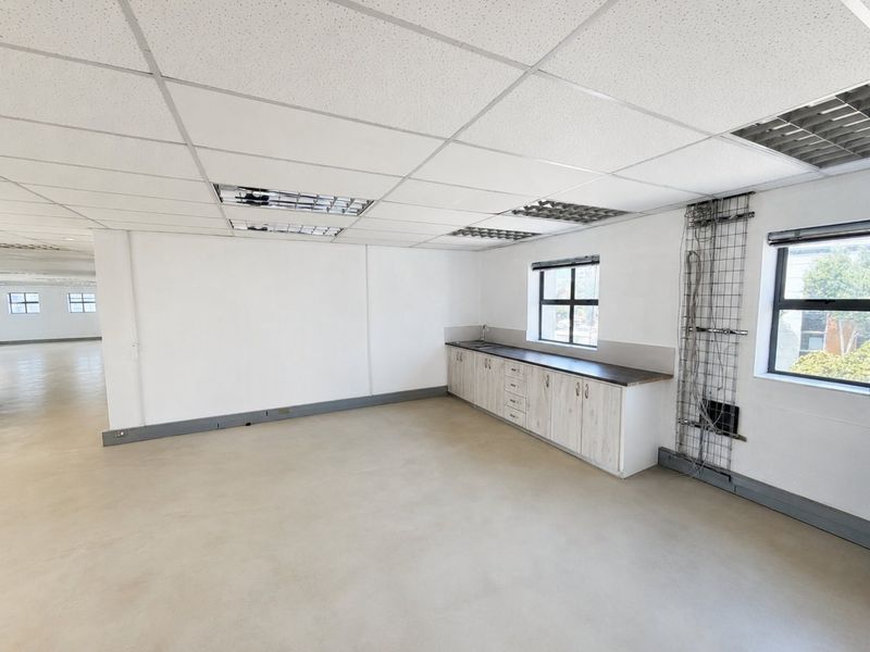 Open-plan commercial office space featuring a built-in kitchenette, polished concrete floors, and suspended ceiling with recessed lighting.