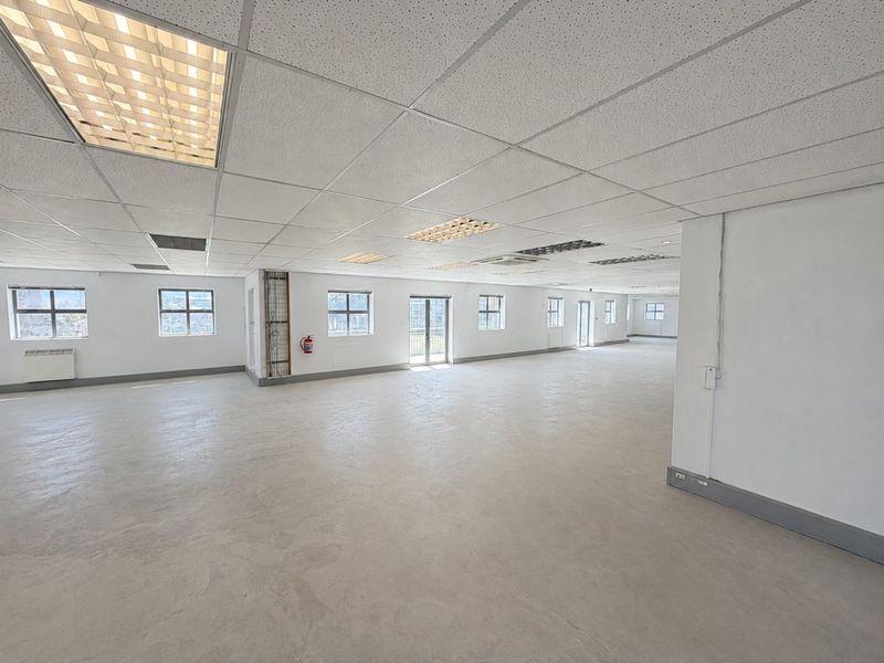 A spacious, open-plan commercial office area featuring a suspended ceiling, recessed lighting, and large windows providing ample natural light.