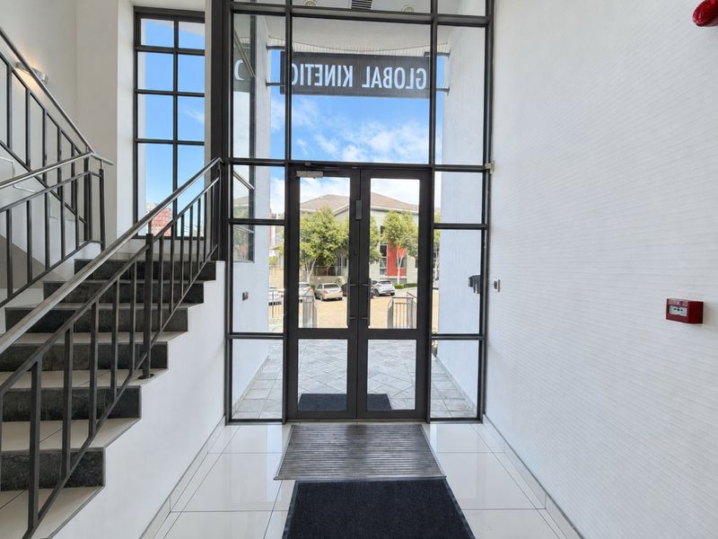 Bright and modern commercial entrance lobby featuring double glass doors, tiled flooring, and a metal staircase leading to upper levels.
