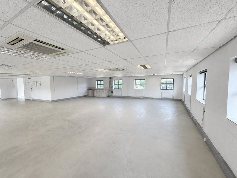 A spacious, open-plan commercial office area featuring a suspended ceiling, recessed lighting, integrated air conditioning, and a small kitchenette corner.