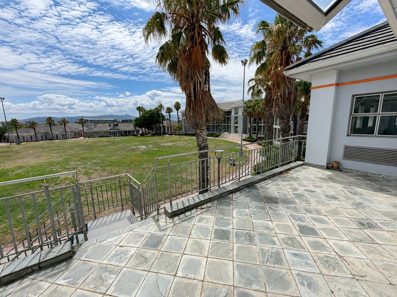 Spacious outdoor patio featuring stone tile flooring and metal balustrades, offering direct access to the surrounding landscaped grounds and communal area.