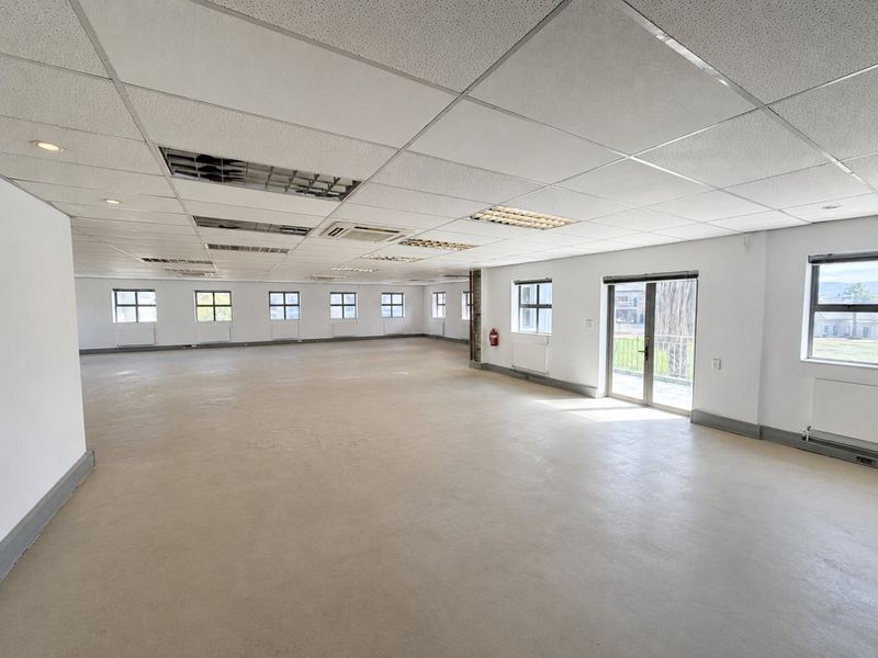 Spacious open-plan commercial office area featuring a suspended ceiling, recessed lighting, ducted air conditioning, and large windows providing ample natural light.