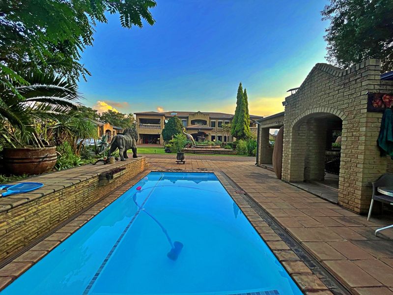 A well-maintained outdoor pool area featuring a paved patio, covered entertainment space, and established garden surroundings, ideal for farm-style outdoor living.