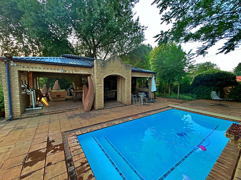 Outdoor entertainment area featuring a swimming pool and a spacious covered brick patio, ideal for relaxation and hosting guests in a garden setting.