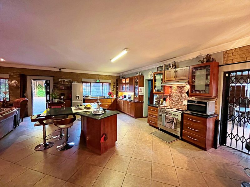 Spacious open-plan kitchen featuring wooden cabinetry, a central island with breakfast bar, gas stove, and tiled flooring, seamlessly connecting to the living area.