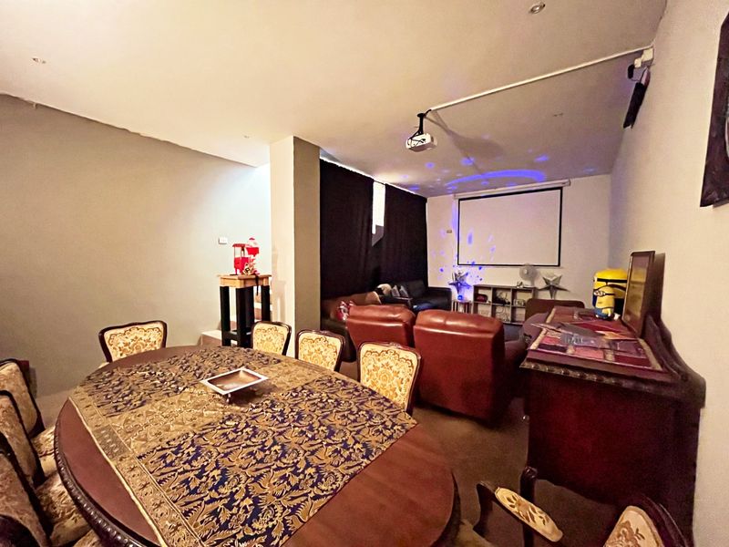 A dedicated cinema room featuring a mounted projector and large projection screen, currently utilized as a multi-purpose entertainment and dining space.