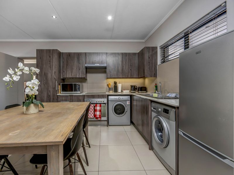 Modern kitchen featuring dark wood cabinetry, stone countertops, integrated appliances, and tiled flooring, offering a functional and contemporary cooking space.
