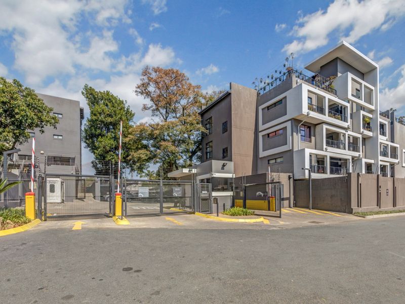 Modern apartment complex entrance featuring secure gated access, electric fencing, a guard house, and multi-level residential units with private balconies.