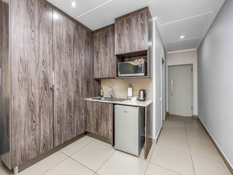 Compact scullery area featuring wood-grain built-in cabinetry, a stainless steel sink, and integrated microwave, finished with neutral floor tiles.