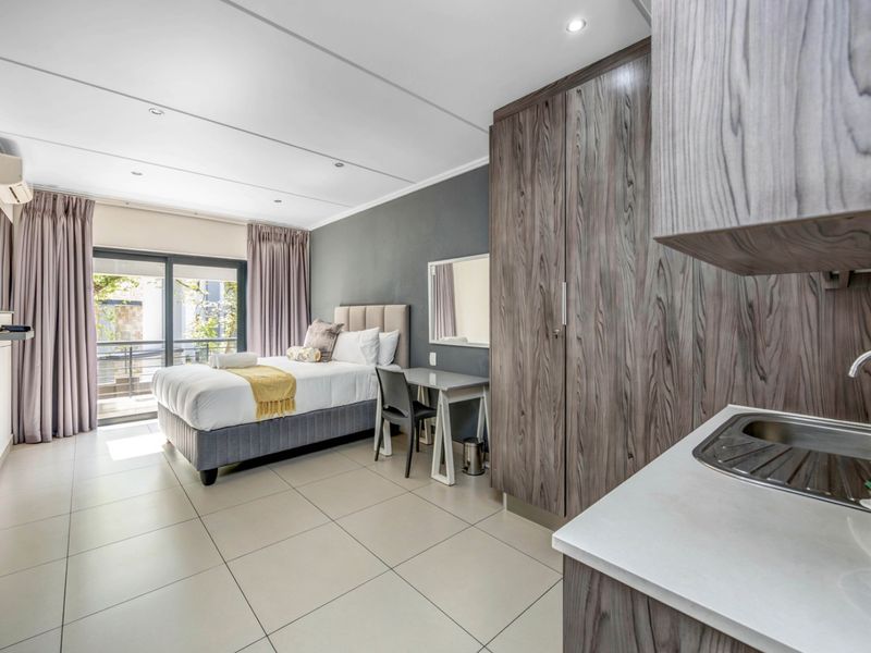 Modern open-plan studio apartment featuring a kitchenette, built-in wardrobe, tiled flooring, and direct access to a private balcony through sliding glass doors.