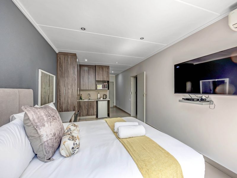 A modern bedroom featuring a compact kitchenette with built-in cabinetry, a wall-mounted air conditioning unit, and recessed ceiling lighting.