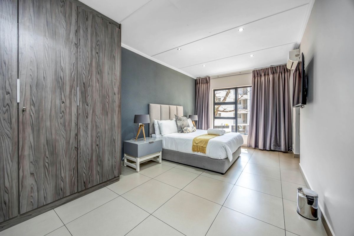 A well-maintained bedroom featuring large built-in cupboards, neutral tiled flooring, recessed lighting, and an air conditioning unit for climate control.