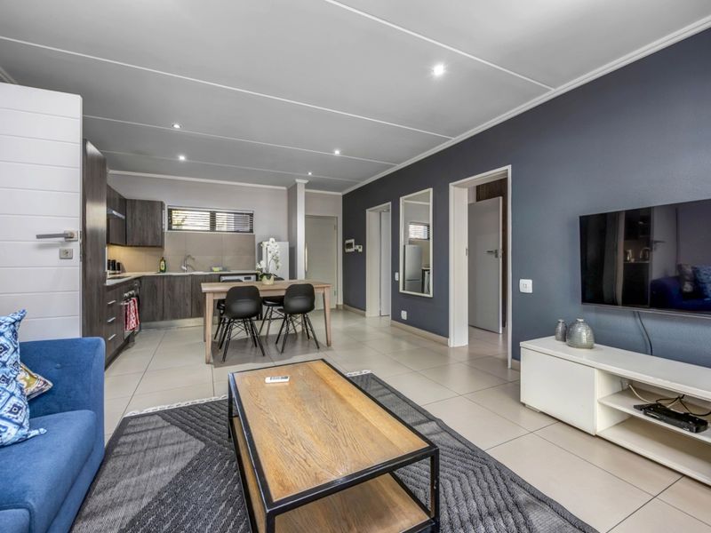 Modern open-plan living area featuring a well-appointed kitchen with built-in cabinetry, tiled floors, and recessed lighting, seamlessly flowing into the lounge space.