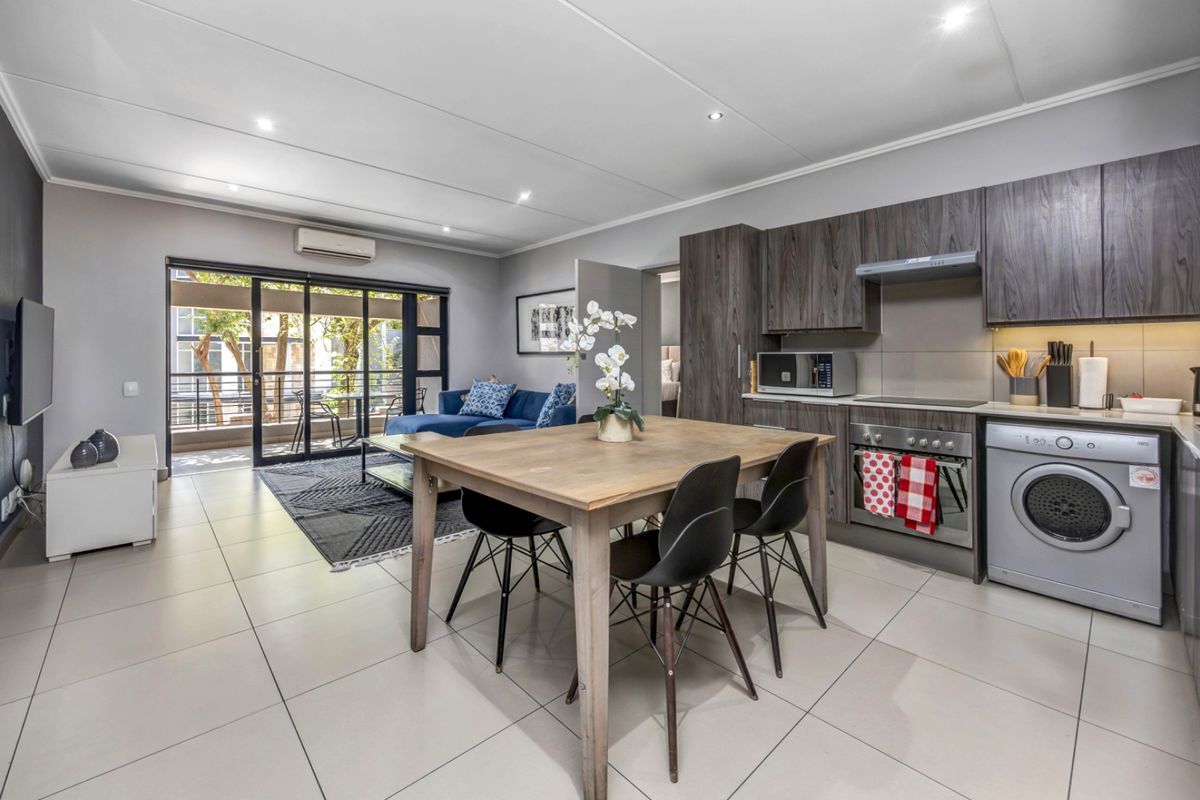 Modern open-plan living area featuring a contemporary kitchen with built-in appliances, tiled flooring, and seamless access to a private balcony.